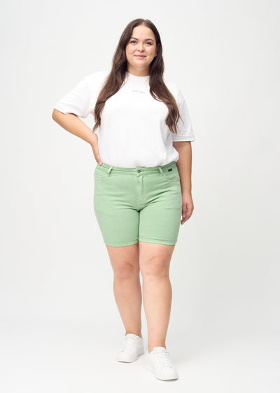 Fuldt billede af en plus-size model i lysegrønne skinny short shorts.