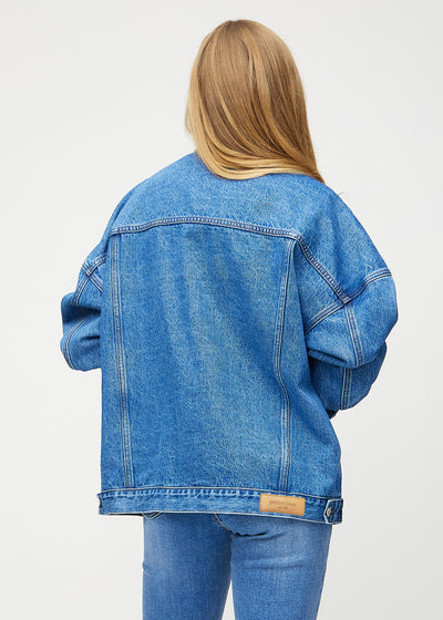 Kvindelig model i blå denim jakke, set bagfra, fremhæver detaljerne på ryggen i farven Rivers.